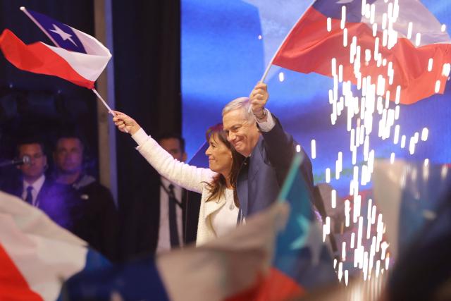 Chile's presidential candidate Jose Antonio Kast, of the Partido Republicano party, and his wife Maria Pia Adriasola wave national flags as they celebrate the results of the presidential runoff election in Santiago on December 14, 2025. Chilean voters elected Jose Antonio Kast, the most right-wing president in 35 years of democracy, with a thumping 58 percent of votes and his rival Jeannette Jara conceding defeat, according to official results on December 14, 2025. (Photo by Javier TORRES / AFP)