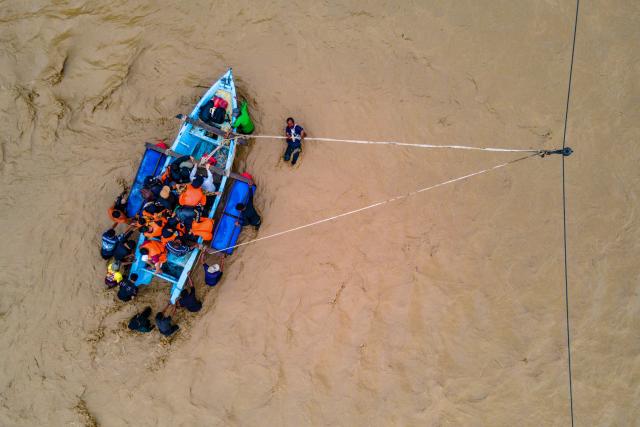 This picture shows an aerial view of residents crossing a river in a boat after a bridge was damaged by flooding in Juli, in Indonesia's Aceh province on December 14, 2025. Devastating floods and landslides have killed 1,006 people in Indonesia, rescuers said December 13 as the Southeast Asian nation grapples with the huge scale of relief efforts. (Photo by CHAIDEER MAHYUDDIN / AFP)