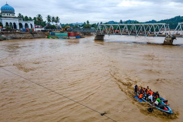 This picture shows an aerial view of residents crossing a river in a boat after a bridge was damaged by flooding in Juli, in Indonesia's Aceh province on December 14, 2025. Devastating floods and landslides have killed 1,006 people in Indonesia, rescuers said December 13 as the Southeast Asian nation grapples with the huge scale of relief efforts. (Photo by CHAIDEER MAHYUDDIN / AFP)