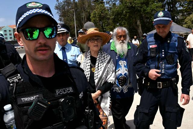 A pro-Palestinian supporter is escorted by police from the Bondi Beach area in Sydney on December 15, 2025, a day after the shootings. A father-and-son team toting long-barrelled guns shot and killed 15 people including a 10-year-old girl at Sydney's Bondi Beach on December 14, with authorities labelling it an antisemitic terrorist attack on a Jewish festival. (Photo by Saeed KHAN / AFP)