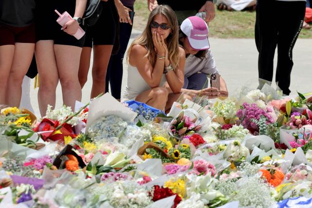 Mourners gather by floral tributes at the Bondi Pavillion in memory of the victims of a shooting at Bondi Beach, in Sydney on December 15, 2025. A father-and-son team toting long-barrelled guns shot and killed 15 people including a 10-year-old girl at Sydney's Bondi Beach on December 14, with authorities labelling it an antisemitic terrorist attack on a Jewish festival. (Photo by DAVID GRAY / AFP)
