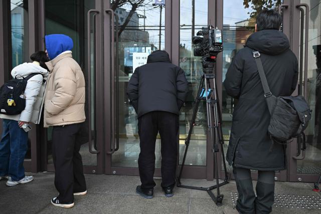 Reporters gather outside the headquarters of Unification Church in Seoul on December 15, 2025, after police raided the building. South Korean police raided the headquarters of the cult-like Unification church on December 15, and named its leader as a suspect in the bribery of several high-profile politicians. (Photo by Jung Yeon-je / AFP)