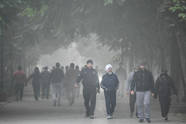 People walk across a garden amid dense smog in Amritsar on December 15, 2025. (Photo by Narinder NANU / AFP)