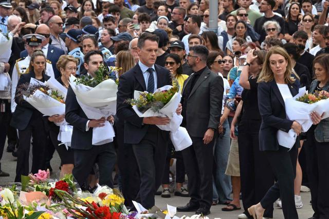 New South Wales Premier Chris Minns (C) and other dignitaries lay flowers as a tribute at the Bondi Pavillion in memory of the victims of a shooting at Bondi Beach, in Sydney on December 15, 2025. A father and son opened fire on a Jewish festival at Australia's Bondi Beach in a shooting spree that killed 15 people, including a child, authorities said on December 15, denouncing the attack as antisemitic "terrorism". (Photo by Saeed KHAN / AFP)