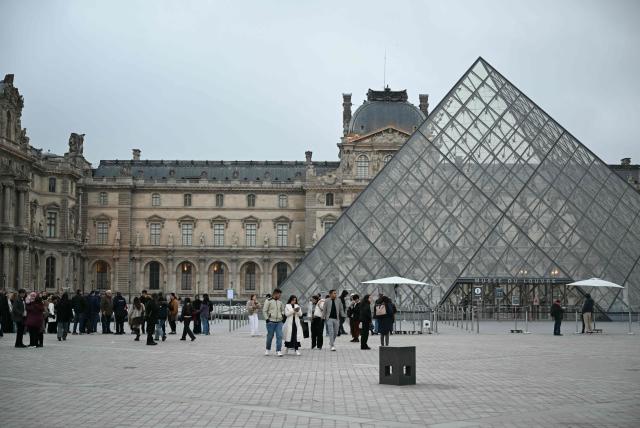 This photograph shows tourists walking in front of the closed Louvre Museum as museum workers meet in a general assembly to vote on unions' call for an open-ended strike against increasingly deteriorating working conditions and the declining visitor experience at the world famous museum in Paris on December 15, 2025. (Photo by Blanca CRUZ / AFP)