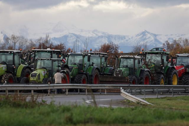 This photograph shows Tractors parked on the A64 motorway with the Pyrenees mountains in the background as part of the fourth day of the blockade in protest against health measures put in place to eradicate lumpy skin disease affecting cattle, in Carbonne, south-western France, on December 15, 2025. (Photo by Valentine CHAPUIS / AFP)