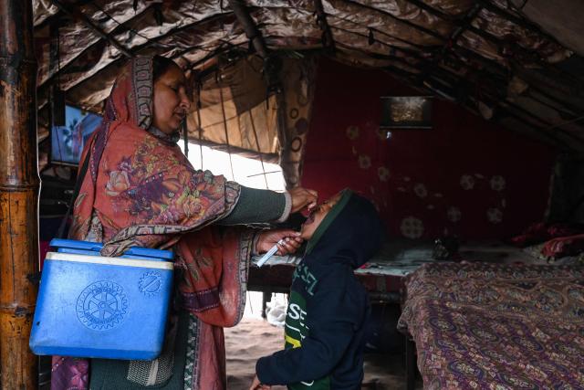 A health worker administers polio drops to a child for vaccination during a door-to-door poliovirus eradication campaign in Lahore on December 15, 2025. (Photo by Arif ALI / AFP)