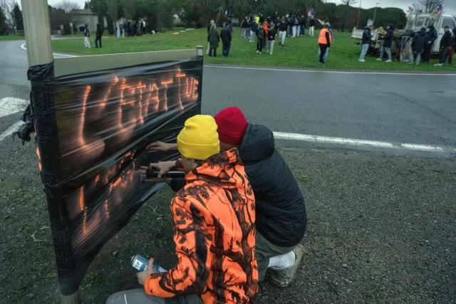 High school students write the message "the state kills" on a banner at a roundabout in front of the Charlemagne agricultural high school during an action in support of farmers protesting against the policy of slaughtering cows with Contagious Nodular Dermatosis (CND) in Carcassonne,  on December 15, 2025. On December 12, 2025 French veterinarians slaughtered a herd of cows thought to be diseased after police dispersed angry farmers trying to protect them, an AFP reporter said, as an agricultural union called for nationwide protests. French farmers are unhappy with the state's management of an outbreak of nodular dermatitis -- widely known as lumpy skin disease. (Photo by Idriss Bigou-Gilles / AFP)