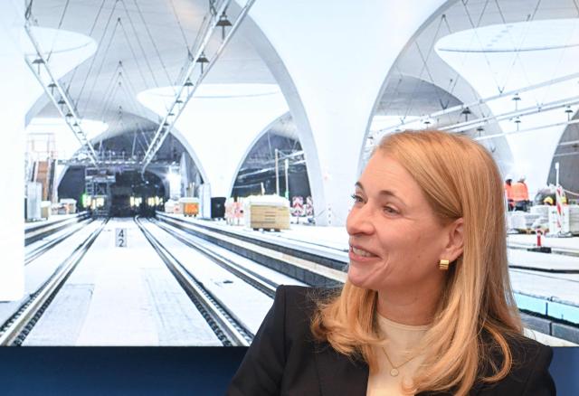 Evelyn Palla, CEO of German railways operator Deutsche Bahn (DB), smiles in front of a photograph of the Stuttgart 21 construction site during a press conference of the Steering Committee on the rail project Stuttgart 21 at the Stuttgart airport in Stuttgart, southern Germany, on December 15, 2025. Palla announced internal investigations, after the inauguration of the mammoth railway project Stuttgart 21 has been delayed yet again. Work began 15 years ago on Stuttgart 21, which involves replacing the current station with a major underground site. But repeated delays have left the city centre resembling a building site, while costs have more than doubled to around 11 billion euros ($12.7 billion). (Photo by THOMAS KIENZLE / AFP)