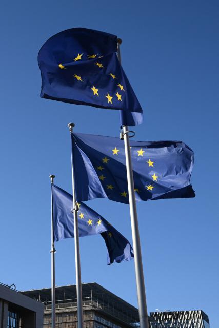 This photograph shows European Union flags outside the Berlaymont building, the headquarters of the European Commission, in Brussels on December 15, 2025. (Photo by Nicolas TUCAT / AFP)