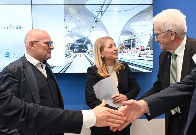 Evelyn Palla (C), CEO of German railways operator Deutsche Bahn (DB), Baden-Wuerttemberg's State Premier Winfried Kretschmann (R) and Baden-Wuerttembergs transport minister Winfried Hermann (L) attend a press conference of the Steering Committee on the rail project Stuttgart 21 at the Stuttgart airport in Stuttgart, southern Germany, on December 15, 2025. Palla announced internal investigations, after the inauguration of the mammoth railway project Stuttgart 21 has been delayed yet again. Work began 15 years ago on Stuttgart 21, which involves replacing the current station with a major underground site. But repeated delays have left the city centre resembling a building site, while costs have more than doubled to around 11 billion euros ($12.7 billion). (Photo by THOMAS KIENZLE / AFP)
