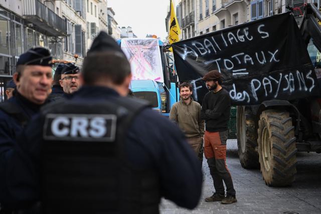 Anti-riot police offficers stand by as farmers protest nearby the Pau Prefecture against the policy of slaughtering cows with Lumpy skin disease, in Pau, southwestern France, on December 15, 2025. The official strategy to stamp out what the authorities describe as a very contagious disease has been to slaughter all animals in affected herds, as well as the "emergency vaccination" of all cattle within a 50-kilometre (30-mile) radius. (Photo by Christophe ARCHAMBAULT / AFP)