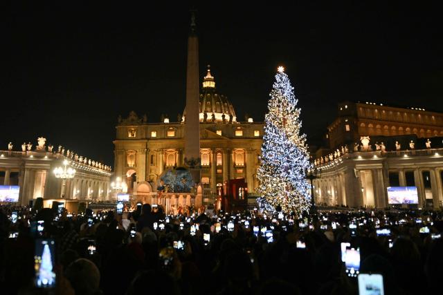 TOPSHOT - People hold their phones to take pictures of christmas illuminations at St Peter's square where the christmas tree and the nativity scene have been inaugurated today in The Vatican on December 15, 2025. (Photo by Tiziana FABI / AFP)