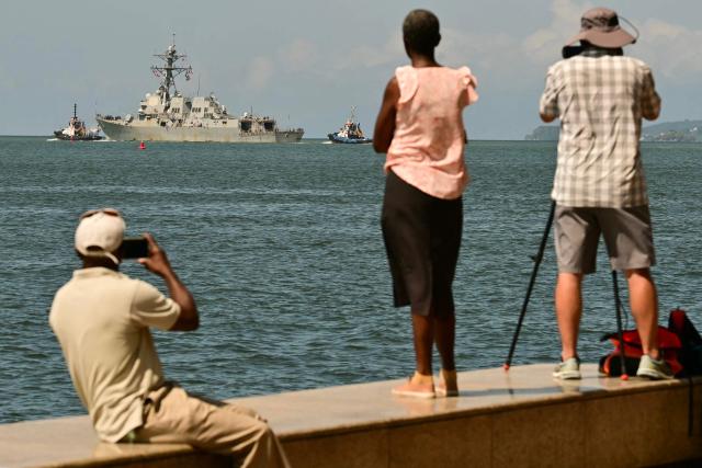 (FILES) People watch and take pictures of the USS Gravely, a US Navy warship, departing the Port of Port of Spain on October 30, 2025. The Caribbean nation of Trinidad and Tobago said on December 15, 2025, it had authorized US military aircraft to use its airports amid growing fears Washington may be preparing an attack on nearby Venezuela. (Photo by MARTIN BERNETTI / AFP)