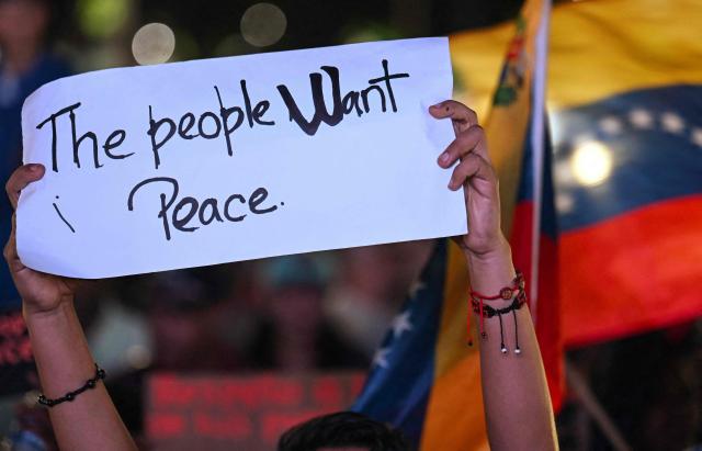 A supporter of Venezuela's President Nicolas Maduro holds a sign during a rally demanding peace in Caracas on December 15, 2025. The Caribbean nation of Trinidad and Tobago said on December 15, 2025, it had authorized US military aircraft to use its airports, amid growing fears Washington may be preparing an attack on nearby Venezuela. (Photo by JUAN BARRETO / AFP)