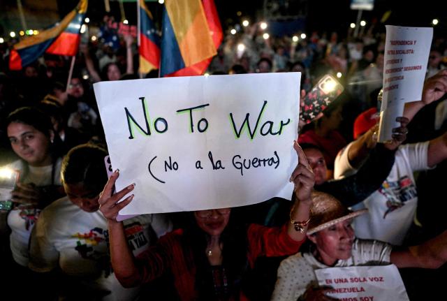 A supporter of Venezuela's President Nicolas Maduro holds a sign during a rally demanding peace in Caracas on December 15, 2025. The Caribbean nation of Trinidad and Tobago said on December 15, 2025, it had authorized US military aircraft to use its airports, amid growing fears Washington may be preparing an attack on nearby Venezuela. (Photo by Juan BARRETO / AFP)