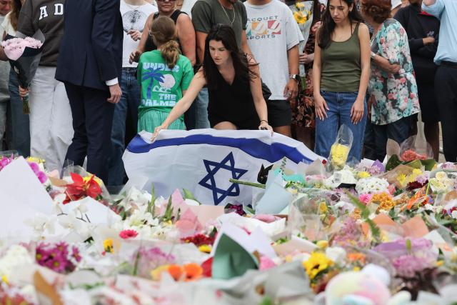 A mourner lays Israel's flag among floral tributes outside Bondi Pavilion in Sydney on December 16, 2025, to honour victims of the Bondi Beach shooting. Australia's leaders have agreed to toughen gun laws after attackers killed 15 people at a Jewish festival on Bondi Beach, the worst mass shooting in decades decried as antisemitic "terrorism" by authorities. (Photo by DAVID GRAY / AFP)