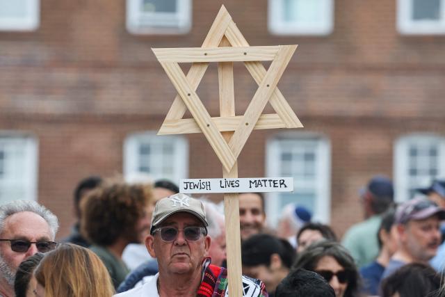 A mourner holds up a wooden Star of David with a sign reading "Jewish Lives Matter" as people gather around floral tributes outside Bondi Pavilion in Sydney on December 16, 2025, to honour victims of the Bondi Beach shooting. Australia's leaders have agreed to toughen gun laws after attackers killed 15 people at a Jewish festival on Bondi Beach, the worst mass shooting in decades decried as antisemitic "terrorism" by authorities. (Photo by DAVID GRAY / AFP)