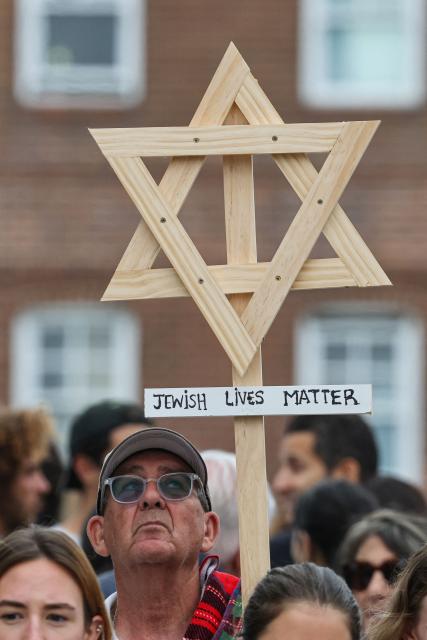 A mourner holds up a wooden Star of David with a sign reading "Jewish Lives Matter" as people gather around floral tributes outside Bondi Pavilion in Sydney on December 16, 2025, to honour victims of the Bondi Beach shooting. Australia's leaders have agreed to toughen gun laws after attackers killed 15 people at a Jewish festival on Bondi Beach, the worst mass shooting in decades decried as antisemitic "terrorism" by authorities. (Photo by DAVID GRAY / AFP)