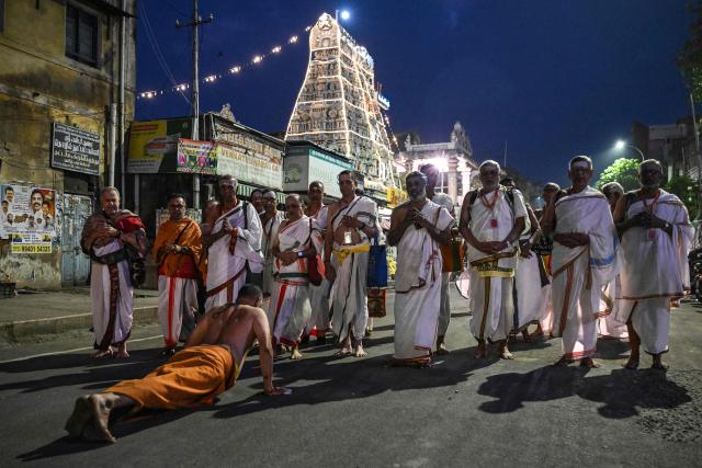 A Hindu devotee seeks blessings from priests as they pray and sing hymns past a temple at the Mylapore neighbourhood early morning in Chennai on December 16, 2025. (Photo by R. Satish BABU / AFP)