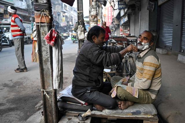 A roadside barber attends to a customer on a cold winter morning in the old quarters of Delhi on December 16, 2025. (Photo by Arun SANKAR / AFP)