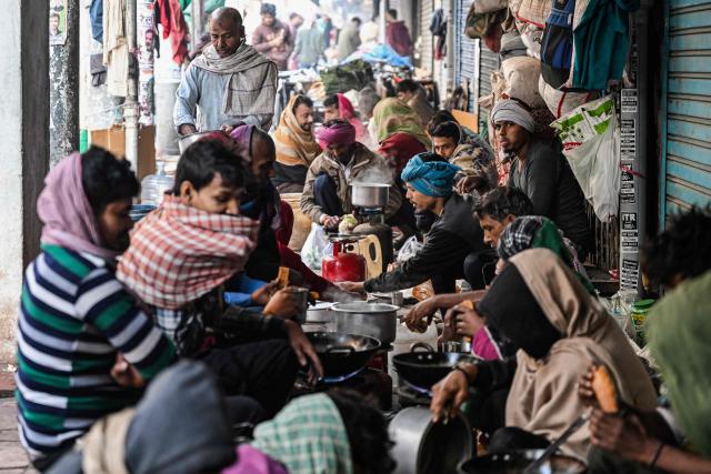 Daily wage workers prepare breakfast along a pavement in the old quaters of Delhi on December 16, 2025. (Photo by Arun SANKAR / AFP)