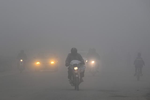 People commute along a street amid dense smog in Lahore on December 16, 2025. (Photo by Arif ALI / AFP)