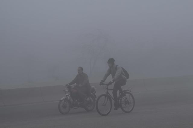 A cyclist wearing an anti-pollution mask rides along a street amid dense smog in Lahore on December 16, 2025. (Photo by Arif ALI / AFP)