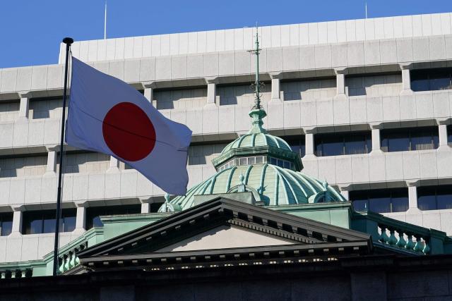 The Japanese flag flutters above the Bank of Japan headquarters in Tokyo on December 16, 2025. The Bank of Japan is expected to hike interest rates on December 19, for the first time since January, pushing them to their highest level in 30 years and potentially exacerbating turmoil in debt markets. (Photo by Kazuhiro NOGI / AFP)