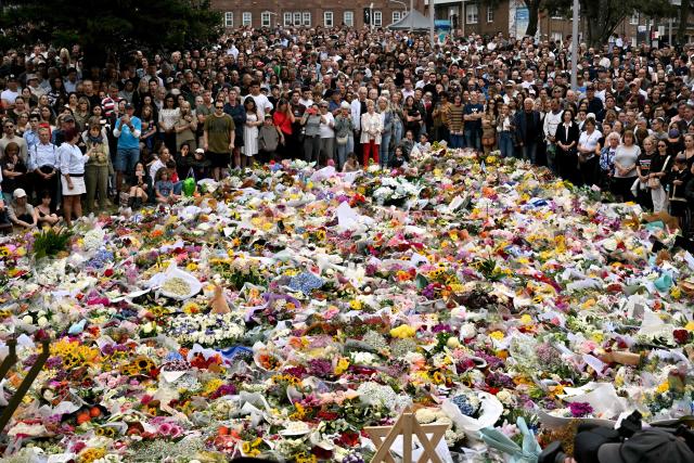 Mourners stand near tributes piled together in memory of the victims of a shooting at Bondi Beach, in Sydney on December 16, 2025. Australia's leaders have agreed to toughen gun laws after attackers killed 15 people at a Jewish festival on Bondi Beach, the worst mass shooting in decades decried as antisemitic "terrorism" by authorities. (Photo by Saeed KHAN / AFP)
