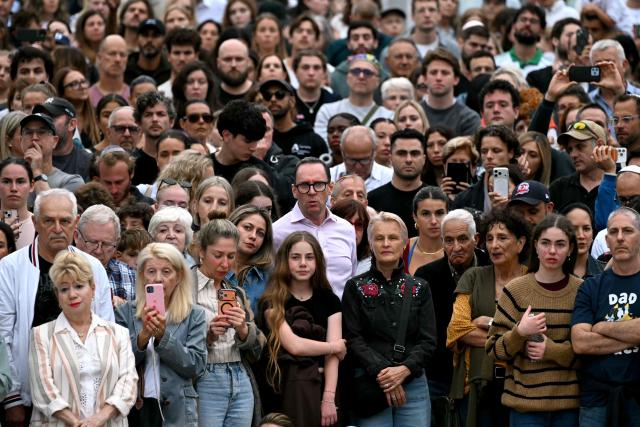 Mourners stand together near tributes at the Bondi Pavilion in memory of the victims of a shooting at Bondi Beach, in Sydney on December 16, 2025. Australia's leaders have agreed to toughen gun laws after attackers killed 15 people at a Jewish festival on Bondi Beach, the worst mass shooting in decades decried as antisemitic "terrorism" by authorities. (Photo by Saeed KHAN / AFP)