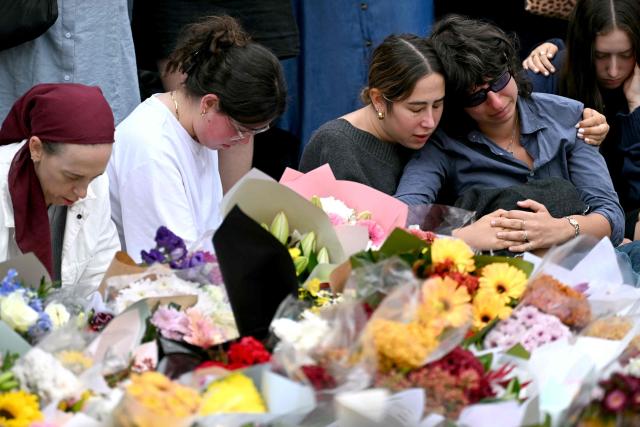 Family members of victims react as they stand with other mourners near tributes at the Bondi Pavilion in memory of the victims of a shooting at Bondi Beach, in Sydney on December 16, 2025. Australia's leaders have agreed to toughen gun laws after attackers killed 15 people at a Jewish festival on Bondi Beach, the worst mass shooting in decades decried as antisemitic "terrorism" by authorities. (Photo by Saeed KHAN / AFP)