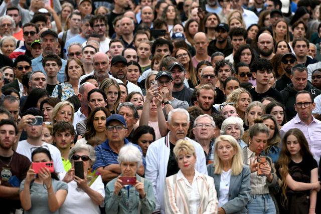 Mourners stand together near tributes at the Bondi Pavilion in memory of the victims of a shooting at Bondi Beach, in Sydney on December 16, 2025. Australia's leaders have agreed to toughen gun laws after attackers killed 15 people at a Jewish festival on Bondi Beach, the worst mass shooting in decades decried as antisemitic "terrorism" by authorities. (Photo by Saeed KHAN / AFP)