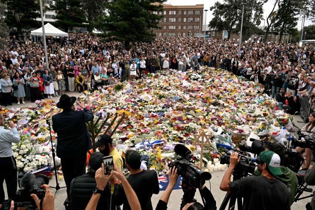 Mourners stand together near tributes at the Bondi Pavilion in memory of the victims of a shooting at Bondi Beach, in Sydney on December 16, 2025. Australia's leaders have agreed to toughen gun laws after attackers killed 15 people at a Jewish festival on Bondi Beach, the worst mass shooting in decades decried as antisemitic "terrorism" by authorities. (Photo by Saeed KHAN / AFP)