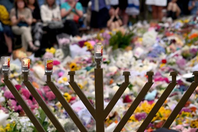 Candles burn in front of mourners as they gather at a tribute at the Bondi Pavilion in memory of the victims of a shooting at Bondi Beach, in Sydney on December 16, 2025. Australia's leaders have agreed to toughen gun laws after attackers killed 15 people at a Jewish festival on Bondi Beach, the worst mass shooting in decades decried as antisemitic "terrorism" by authorities. (Photo by Saeed KHAN / AFP)