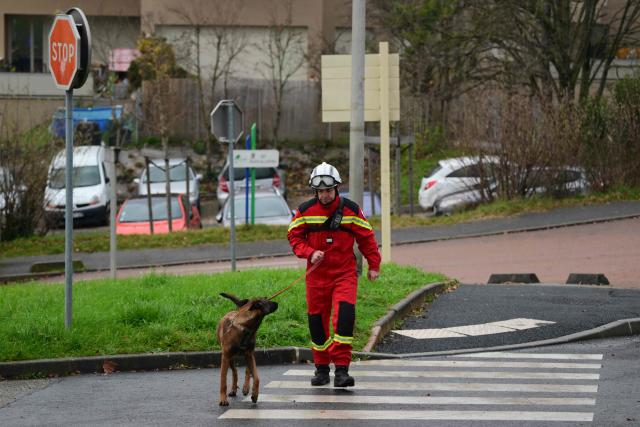 A French firefighter of the Ain department walks with a dog to conduct searches near the site of a residential building explosion in Trevoux on December 16, 2025. Search operations are set to resume December 16 morning in Trévoux, in the Ain department, in the rubble of a residential building where an explosion on December 15 killed two young children and left thirteen people injured. (Photo by Olivier CHASSIGNOLE / AFP)