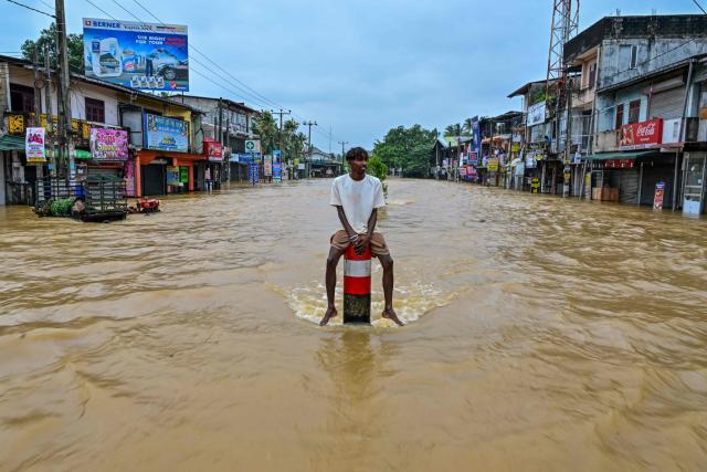 (FILES) A man sits on a divider in the middle of a flooded road after heavy rainfall in Kaduwela on the outskirts of Colombo on November 29, 2025. Global economic losses from natural disasters are projected to have dropped by 33 percent to $220 billion in 2025, despite the damage wrought by the Los Angeles wildfires, reinsurer Swiss Re said on December 16, 2025. The total cost of insured losses from natural catastrophes is estimated at $107 billion, down 24 percent from the previous year, the Zurich-based reinsurance giant said in its preliminary estimates for 2025. (Photo by Ishara S. KODIKARA / AFP)