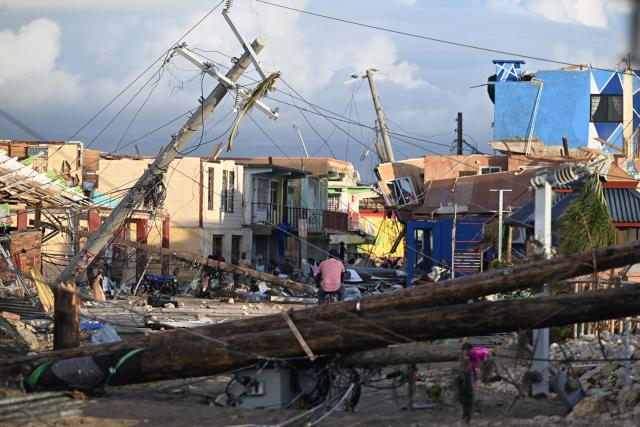 (FILES) Electrical poles are down as a man bikes through the destroyed neighborood of North Street following the passage of Hurricane Melissa, in Black River, Jamaica on October 29, 2025. Global economic losses from natural disasters are projected to have dropped by 33 percent to $220 billion in 2025, despite the damage wrought by the Los Angeles wildfires, reinsurer Swiss Re said on December 16, 2025. The total cost of insured losses from natural catastrophes is estimated at $107 billion, down 24 percent from the previous year, the Zurich-based reinsurance giant said in its preliminary estimates for 2025. (Photo by Ricardo MAKYN / AFP)