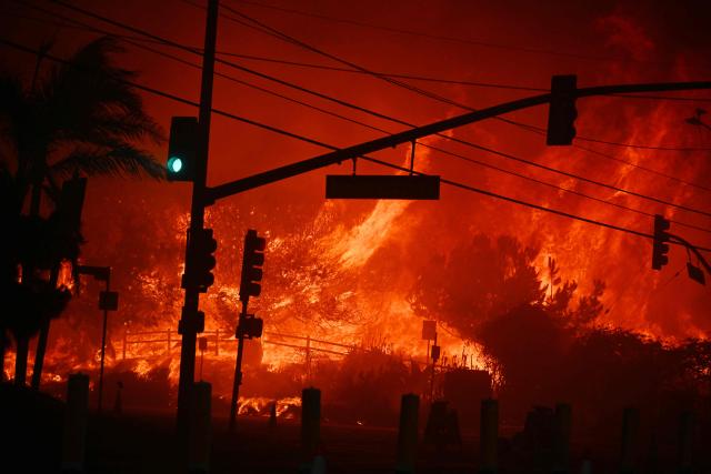 (FILES) Flames overtake the intersection of Temescal Canyon and Pacific Coast Highway Fire at the Palisades Fire in Pacific Palisades California on January 7, 2025. Global economic losses from natural disasters are projected to have dropped by 33 percent to $220 billion in 2025, despite the damage wrought by the Los Angeles wildfires, reinsurer Swiss Re said on December 16, 2025. The total cost of insured losses from natural catastrophes is estimated at $107 billion, down 24 percent from the previous year, the Zurich-based reinsurance giant said in its preliminary estimates for 2025. (Photo by Robyn Beck / AFP)