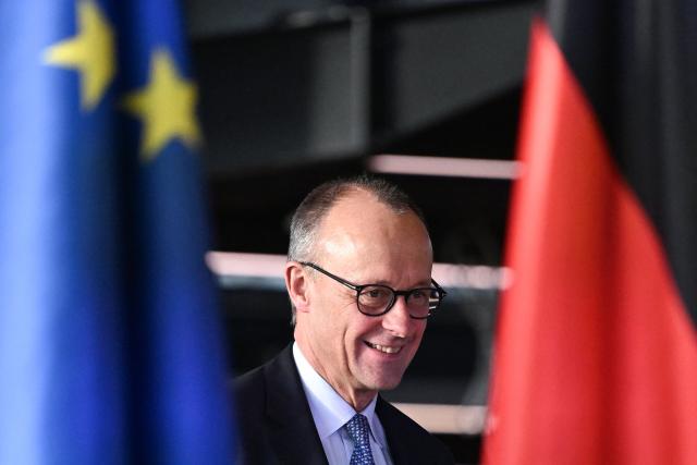 German Chancellor Friedrich Merz is seen between a German (R) and a European flag as he arrives to address a press conference during his visit of the new Terminal 3 at Frankfurt Airport (FRA) in Frankfurt am Main, western Germany on December 16, 2025, as part of his inaugural visit to the German state of Hesse. Fraport will open the new Terminal 3 on April 22, 2026. (Photo by Kirill KUDRYAVTSEV / AFP)