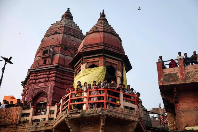 People gather to watch the funeral pyres burning along the banks of the river Ganges at Manikarnika Ghat in Varanasi on December 16, 2025. (Photo by Niharika KULKARNI / AFP)
