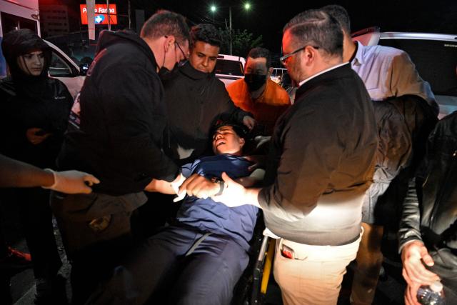 A supporter of the ruling Libertad y Refundacion (LIBRE) party, who was injured during an eviction by the National Civil Police and the Military Police of Public Order (PMOP), is assisted in the surroundings of the National Institute of Professional Training (INFOP), where the National Electoral Council (CNE) will carry out the scrutiny, after the vote count was interrupted several times due to computer failures, in Tegucigalpa on December 16, 2025. At least eight people were injured on Monday night during an operation to remove left-wing militants who were pressing for the final results of the general elections in Honduras, authorities reported on Tuesday. More than two weeks after the elections, Hondurans still do not know the winner of the presidential race or other elected officials in positions such as mayor of the capital, Tegucigalpa. (Photo by Orlando SIERRA / AFP)