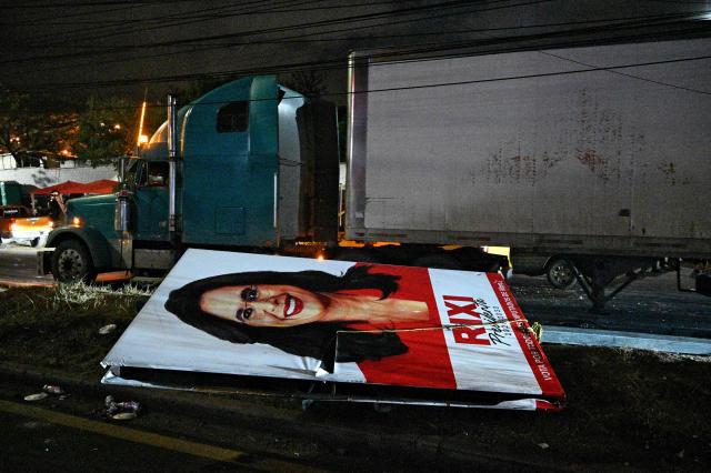 A banner of former Honduras' presidential candidate Rixi Moncada, for the Libertad y Refundacion (LIBRE) party, is seen on the floor after an eviction by the National Civil Police and the Military Police of Public Order (PMOP), in the surroundings of the National Institute of Professional Training (INFOP), where the National Electoral Council (CNE) will carry out the scrutiny, after the vote count was interrupted several times due to computer failures, in Tegucigalpa on December 16, 2025. At least eight people were injured on Monday night during an operation to remove left-wing militants who were pressing for the final results of the general elections in Honduras, authorities reported on Tuesday. More than two weeks after the elections, Hondurans still do not know the winner of the presidential race or other elected officials in positions such as mayor of the capital, Tegucigalpa. (Photo by Orlando SIERRA / AFP)