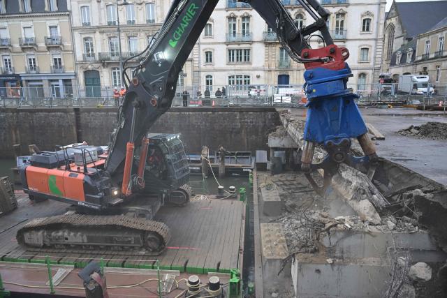 Workers use an excavator, mounted on a barge, to chip away the slab of a car park and uncover the Vilaine river, in the city centre of Rennes, western France on December 16, 2025. (Photo by Damien MEYER / AFP)