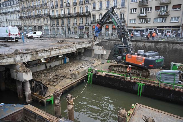 Workers use an excavator, mounted on a barge, to chip away the slab of a car park and uncover the Vilaine river, in the city centre of Rennes, western France on December 16, 2025. (Photo by Damien MEYER / AFP)