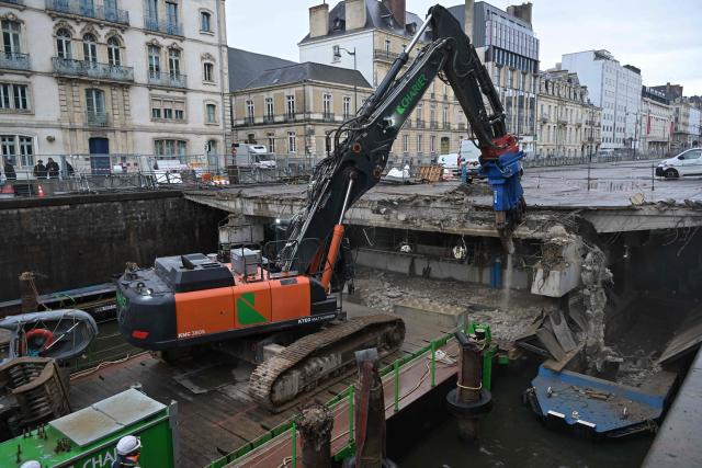 Workers use an excavator, mounted on a barge, to chip away the slab of a car park and uncover the Vilaine river, in the city centre of Rennes, western France on December 16, 2025. (Photo by Damien MEYER / AFP)