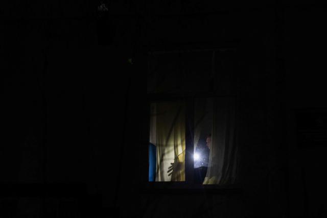 A man with a flashlight closes a window during a blackout in Kyiv on December 16, 2025, amid the Russian invasion of Ukraine. (Photo by Tetiana DZHAFAROVA / AFP)