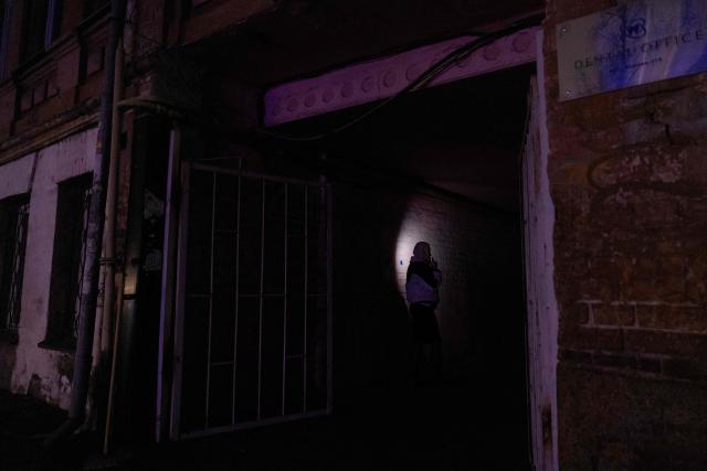 A woman with a flashlight smokes a cigarette on an unlit street during a blackout in Kyiv on December 16, 2025, amid the Russian invasion of Ukraine. (Photo by Tetiana DZHAFAROVA / AFP)