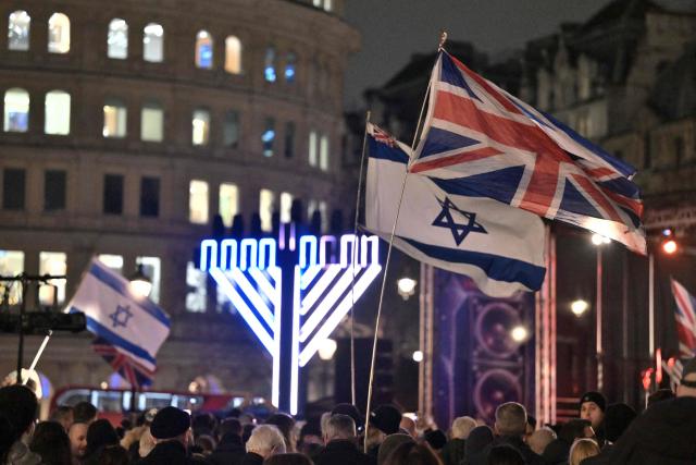 Large Israeli flags are waved as people gather for a "Chanukah LIVE" event for the Jewish festival of Hanukkah at Trafalgar Square in central London on December 16, 2025. The event was held just days after a father and son in Sydney opened fire on crowds gathered for a Jewish festival at Bondi Beach that killed 15 people and wounded dozens. (Photo by Richard A. Brooks / AFP)