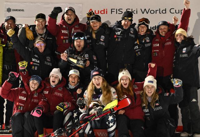 US' Mikaela Shiffrin celebrates with her team on the podium after winning the FIS Alpine Skiing women's World Cup 2025-2026 slalom in Courchevel, French Alps, on December 16, 2025. (Photo by Jeff PACHOUD / AFP)